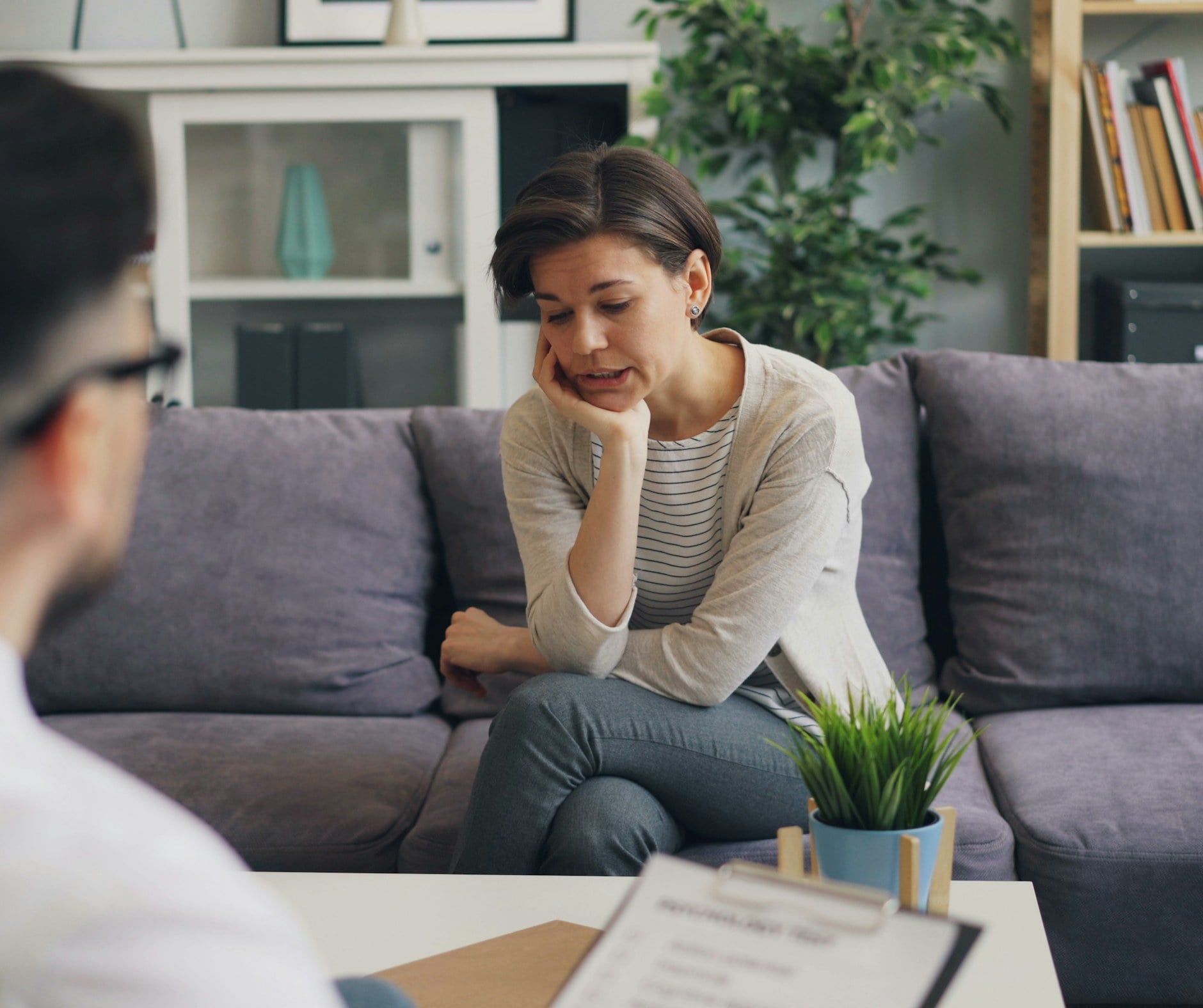 Clinician with a clipboard in a consultation with a woman seated on a sofa